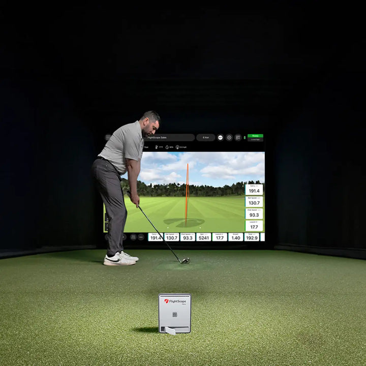A golfer prepares to swing in a high-tech indoor golf setting, with performance metrics displayed in real time.